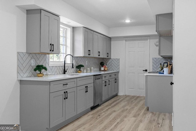 kitchen with gray cabinetry, stainless steel dishwasher, light wood-type flooring, and tasteful backsplash