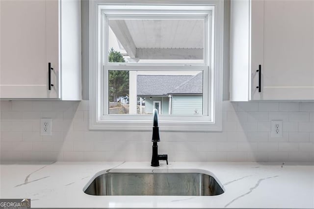 room details with white cabinets, decorative backsplash, light stone countertops, and sink