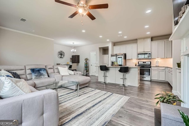 living room with ceiling fan with notable chandelier, light hardwood / wood-style floors, and ornamental molding