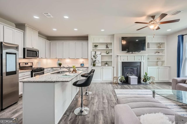 kitchen with white cabinetry, sink, light stone countertops, stainless steel appliances, and a kitchen island with sink