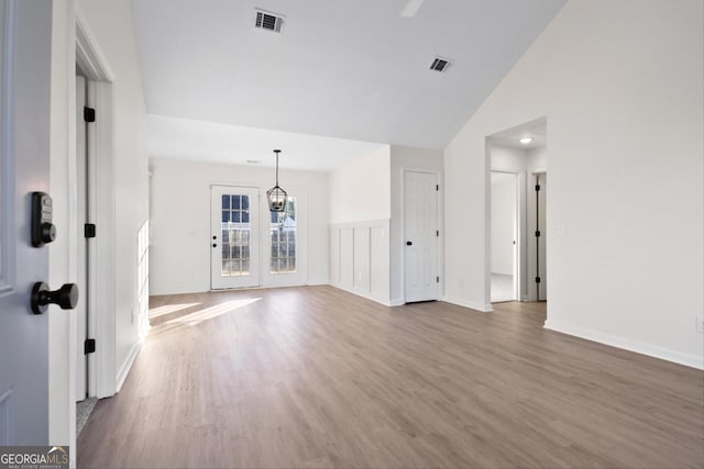 unfurnished living room featuring wood-type flooring, lofted ceiling, and an inviting chandelier