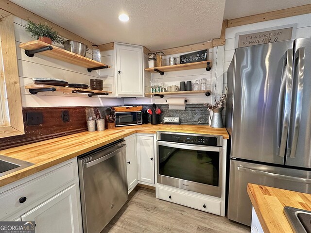 kitchen with white cabinets, a textured ceiling, appliances with stainless steel finishes, and wooden counters