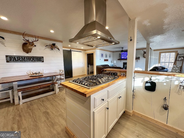 kitchen featuring a barn door, wooden counters, a textured ceiling, white cabinets, and exhaust hood