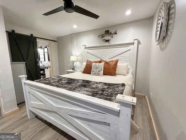 bedroom with a barn door, hardwood / wood-style flooring, and ceiling fan