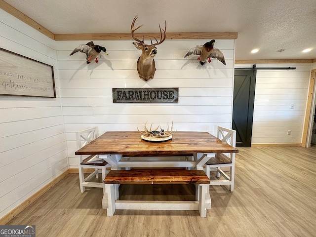 dining area with light wood-type flooring, a textured ceiling, a barn door, and wood walls