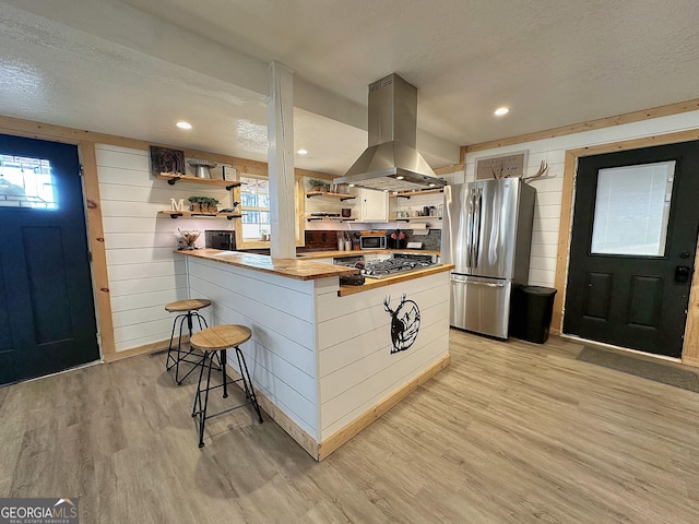 kitchen featuring stainless steel appliances, light hardwood / wood-style flooring, kitchen peninsula, wood walls, and island range hood