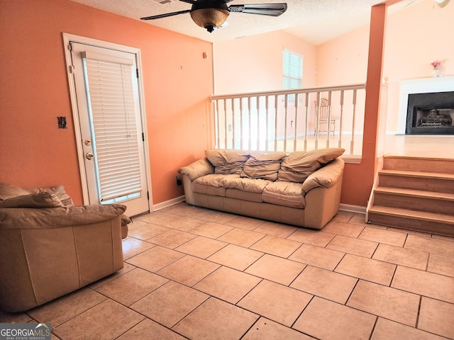 living area featuring light tile patterned floors, baseboards, a ceiling fan, and a textured ceiling