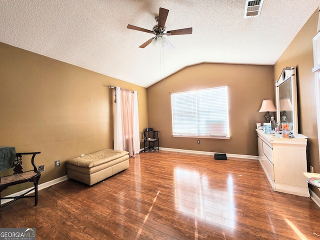 living area with a ceiling fan, wood-type flooring, visible vents, and vaulted ceiling