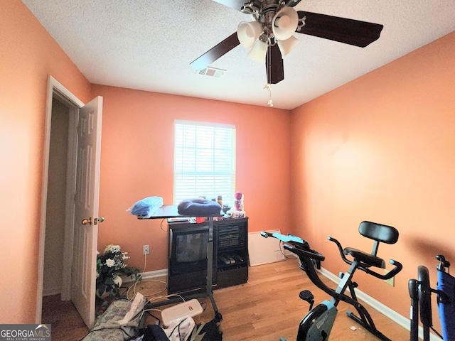 exercise area with a textured ceiling, visible vents, baseboards, a ceiling fan, and light wood finished floors