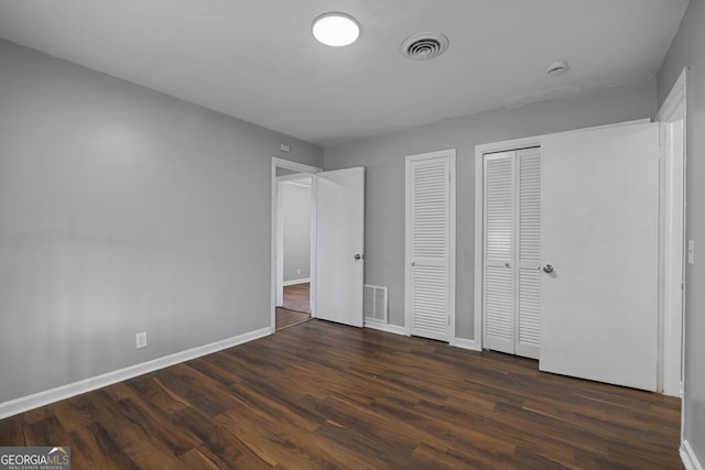 unfurnished bedroom featuring dark wood-type flooring and two closets