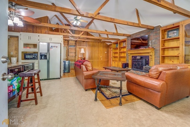 living room with a wood stove, ceiling fan, beam ceiling, built in shelves, and wood walls