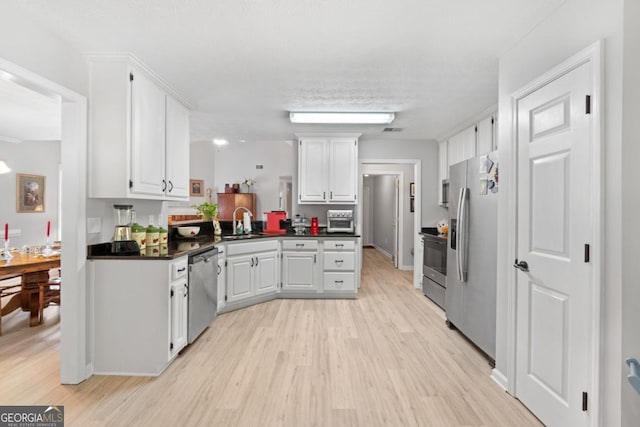 kitchen featuring sink, light wood-type flooring, white cabinetry, kitchen peninsula, and stainless steel appliances