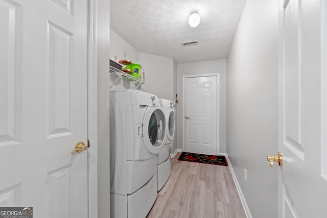 clothes washing area featuring washer and clothes dryer, a textured ceiling, and light wood-type flooring