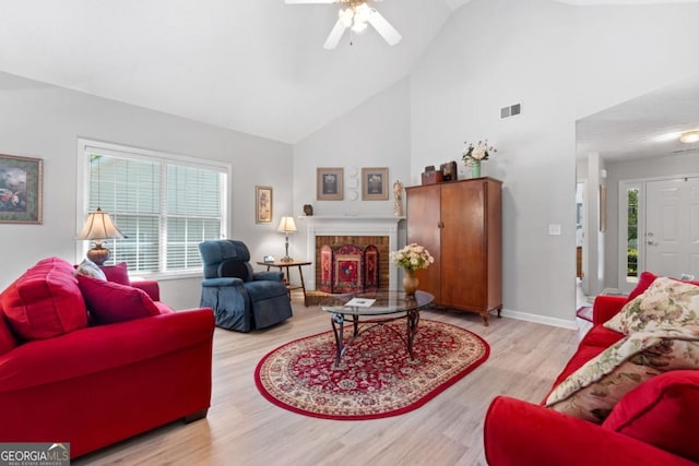 living room with ceiling fan, light hardwood / wood-style flooring, high vaulted ceiling, and a brick fireplace