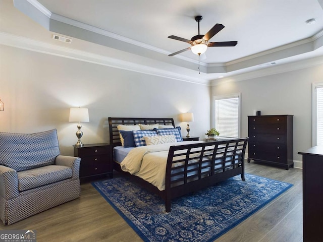 bedroom with hardwood / wood-style floors, ceiling fan, a raised ceiling, and ornamental molding