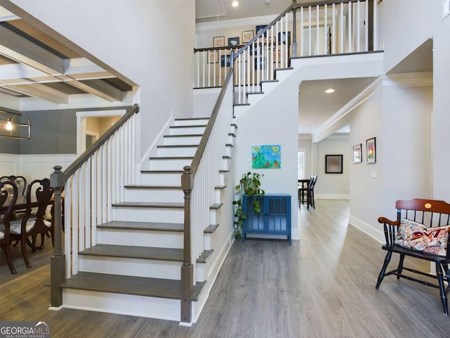 stairway with beam ceiling, hardwood / wood-style flooring, coffered ceiling, and ornamental molding