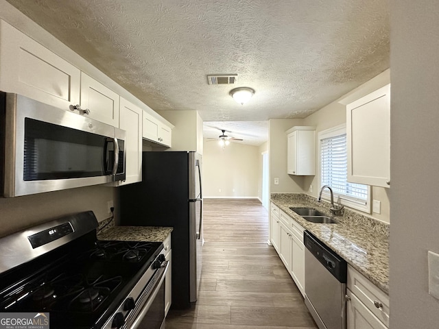 kitchen featuring hardwood / wood-style floors, white cabinets, sink, appliances with stainless steel finishes, and light stone counters