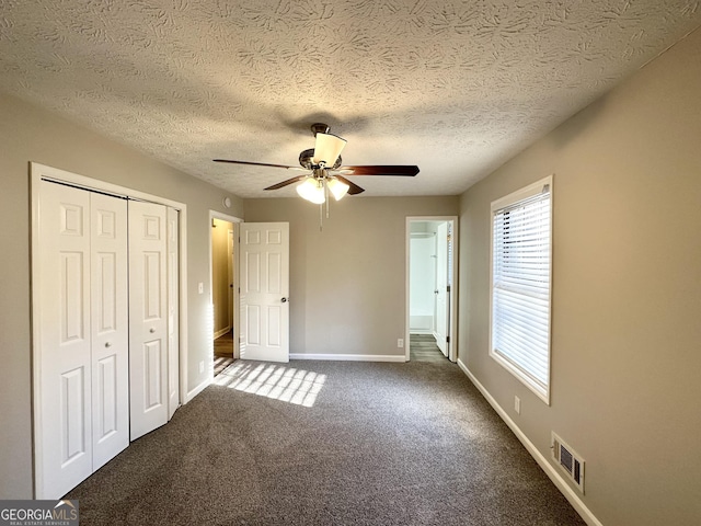 unfurnished bedroom with ceiling fan, dark carpet, and a textured ceiling