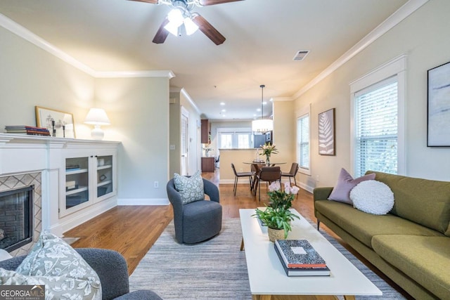 living room with a tiled fireplace, ceiling fan, light wood-type flooring, and ornamental molding