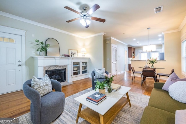 living room featuring a tiled fireplace, crown molding, light hardwood / wood-style floors, and ceiling fan with notable chandelier