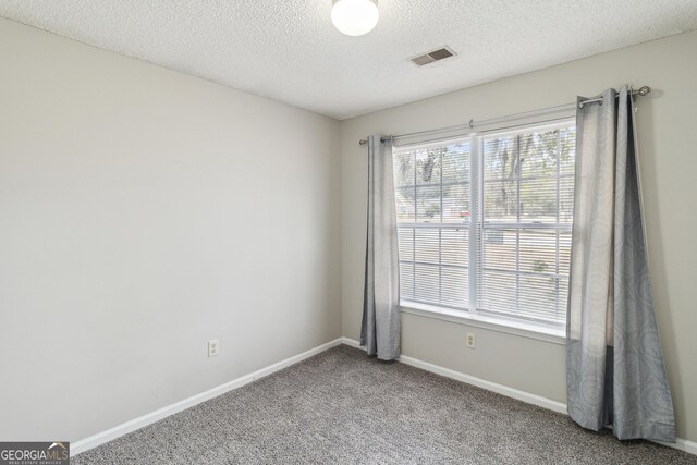 carpeted spare room featuring baseboards, visible vents, and a textured ceiling