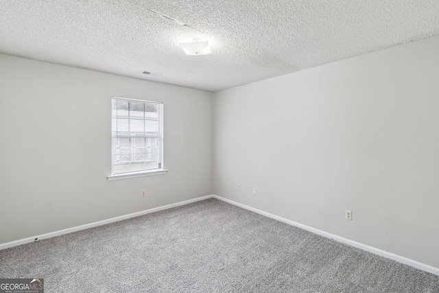 carpeted spare room featuring a textured ceiling, visible vents, and baseboards