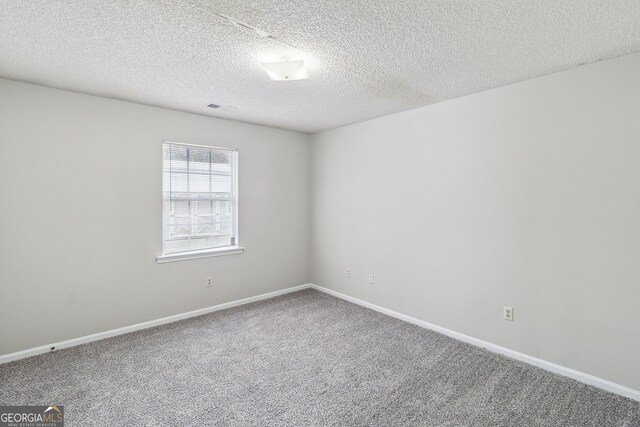 carpeted spare room featuring a textured ceiling, visible vents, and baseboards