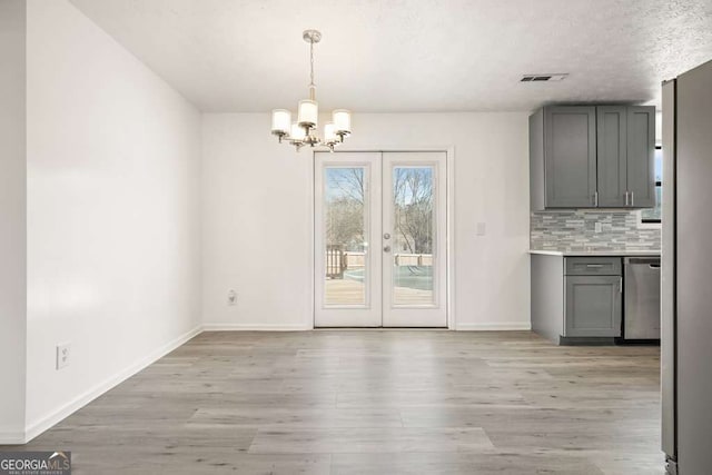 unfurnished dining area with a textured ceiling, a chandelier, light hardwood / wood-style flooring, and french doors