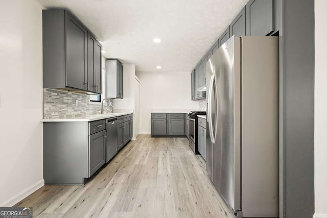 kitchen with appliances with stainless steel finishes, light wood-type flooring, backsplash, sink, and gray cabinets