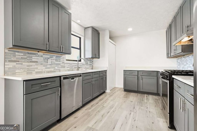 kitchen featuring light wood-type flooring, stainless steel appliances, gray cabinets, and backsplash