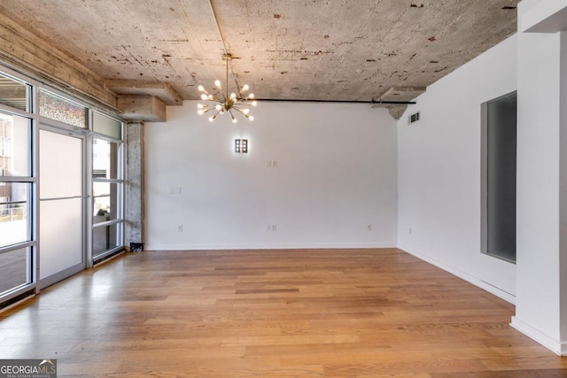 empty room with a wealth of natural light, an inviting chandelier, and light wood-type flooring