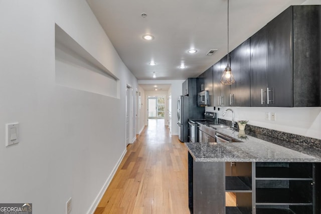 kitchen with sink, stainless steel appliances, kitchen peninsula, dark stone countertops, and light wood-type flooring