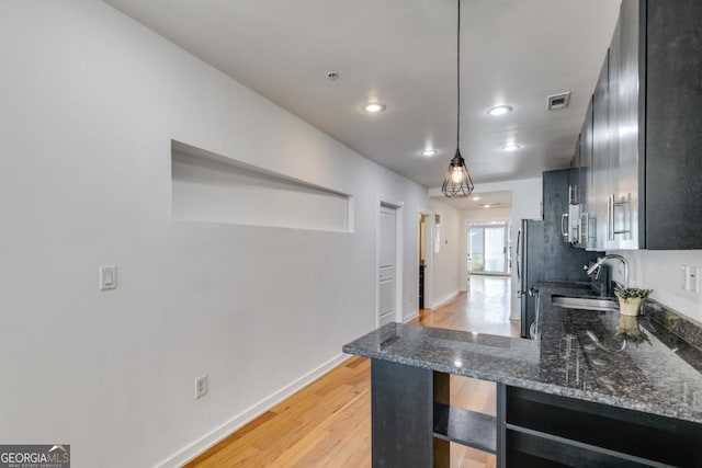 kitchen featuring dark stone counters, hanging light fixtures, light hardwood / wood-style flooring, kitchen peninsula, and stainless steel appliances