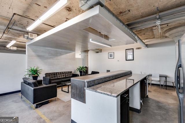 kitchen with stainless steel fridge, a kitchen island, and concrete flooring