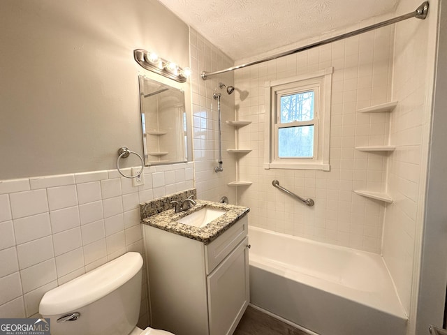 full bathroom with tiled shower / bath combo, a textured ceiling, toilet, vanity, and tile walls