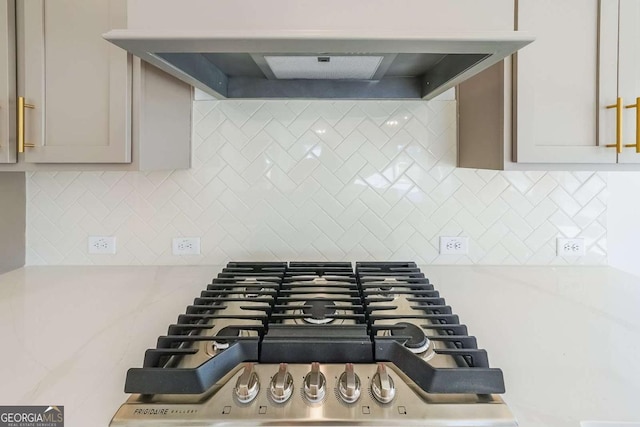 details featuring backsplash, light stone countertops, exhaust hood, and stainless steel gas stovetop