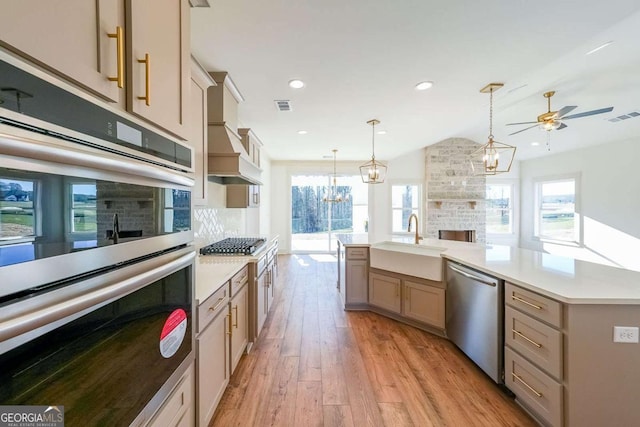 kitchen with sink, decorative light fixtures, a fireplace, ceiling fan with notable chandelier, and appliances with stainless steel finishes