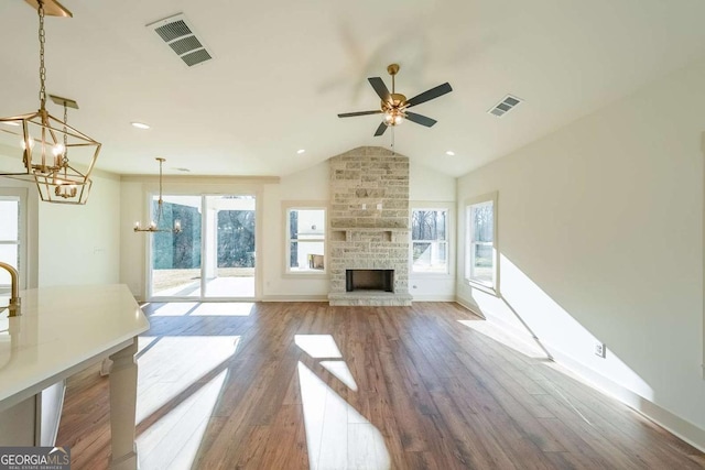 unfurnished living room featuring vaulted ceiling, a stone fireplace, ceiling fan with notable chandelier, and hardwood / wood-style flooring