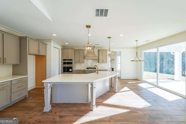 kitchen featuring decorative backsplash, a kitchen island with sink, pendant lighting, hardwood / wood-style flooring, and a breakfast bar area