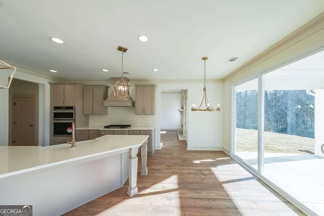 kitchen featuring decorative light fixtures, custom range hood, double oven, and light hardwood / wood-style flooring