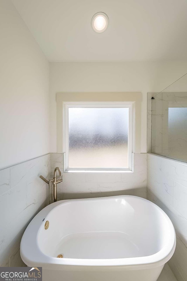 bathroom with a tub, a healthy amount of sunlight, and tile walls