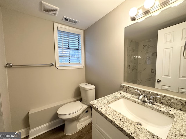 bathroom with tiled shower, wood-type flooring, vanity, and toilet