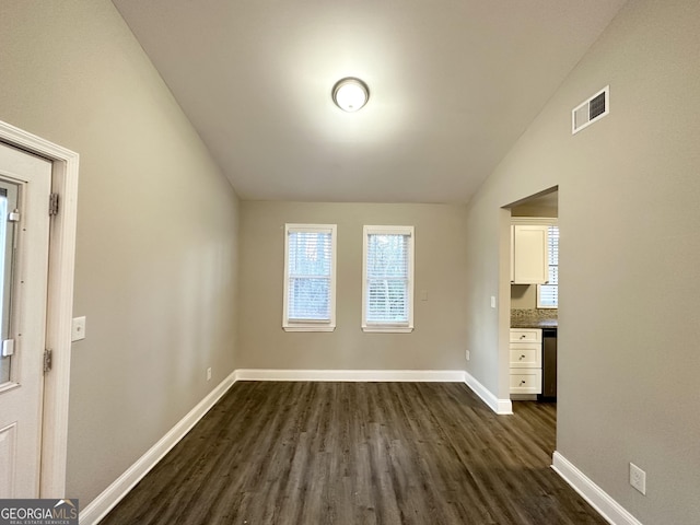 empty room with dark hardwood / wood-style flooring and vaulted ceiling