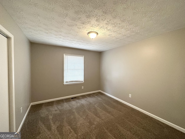 empty room with dark colored carpet and a textured ceiling