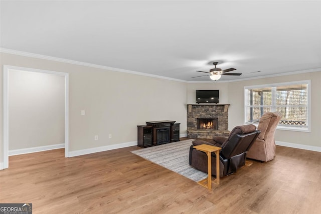 living room with ceiling fan, a stone fireplace, light wood-type flooring, and crown molding