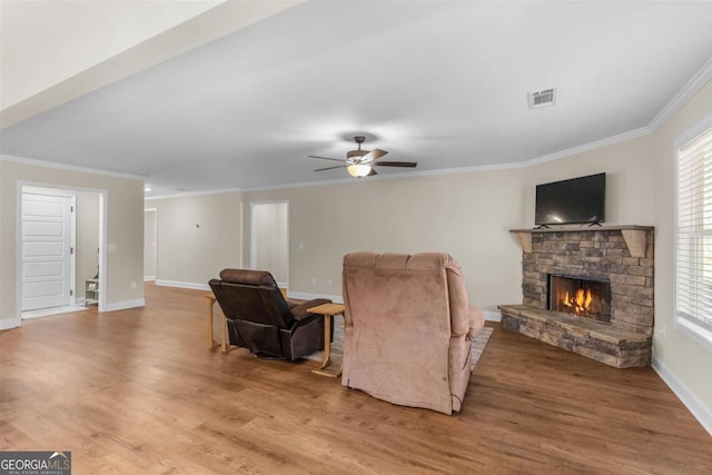 living room with ceiling fan, a stone fireplace, and crown molding