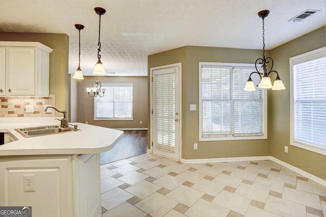 kitchen with pendant lighting, backsplash, sink, white cabinetry, and a chandelier