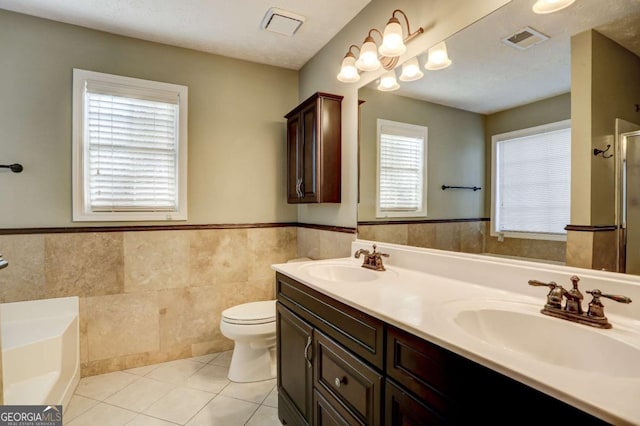 bathroom with vanity, tile patterned flooring, toilet, a tub to relax in, and tile walls