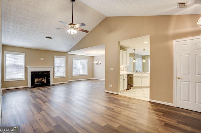 unfurnished living room with a textured ceiling, ceiling fan with notable chandelier, sink, a premium fireplace, and light hardwood / wood-style floors