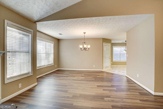 spare room featuring a healthy amount of sunlight, wood-type flooring, a textured ceiling, and a notable chandelier